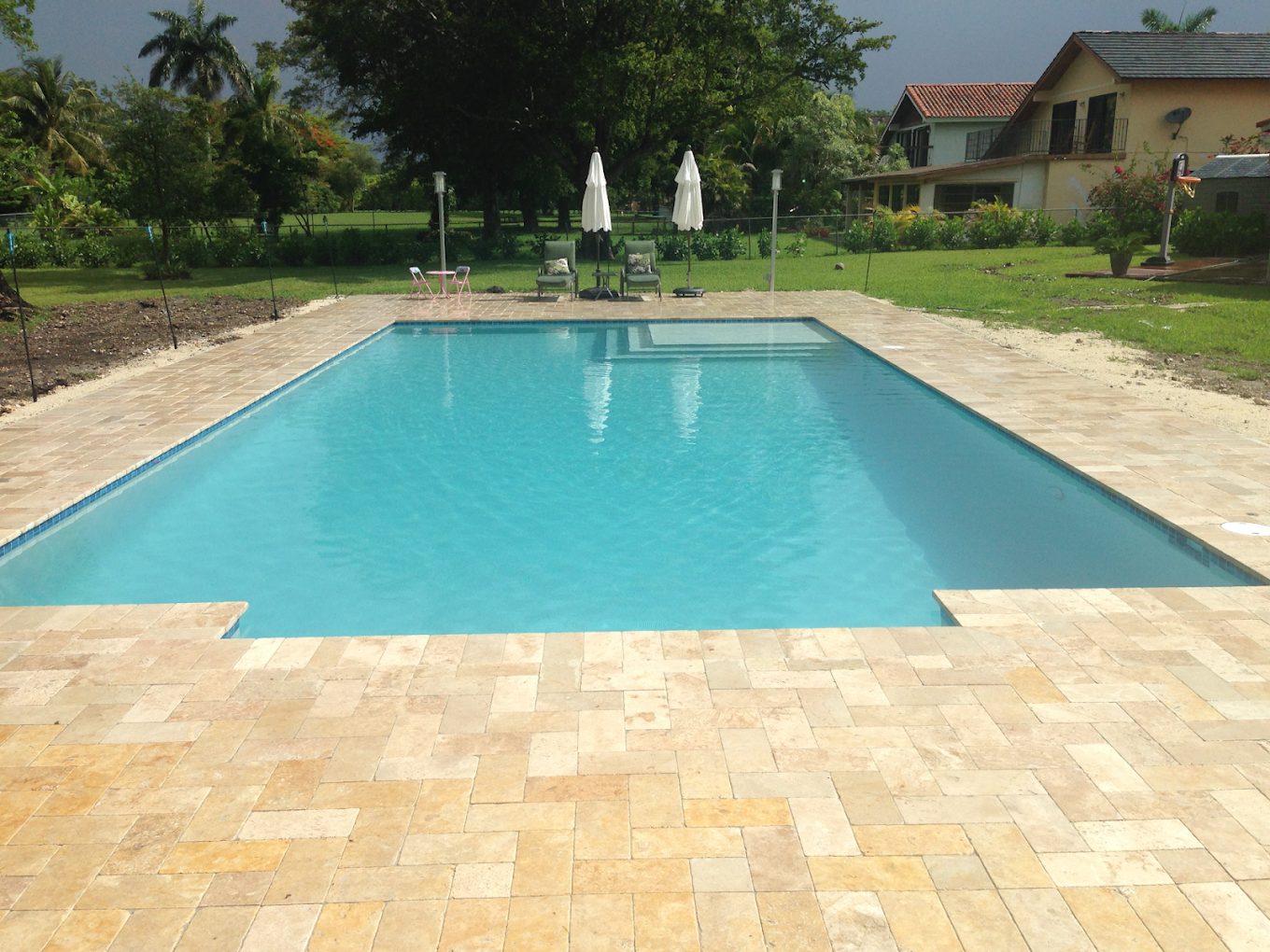 A large custom swimming pool with a travertine deck and lawn, built by Pool Construction Inc in Miami